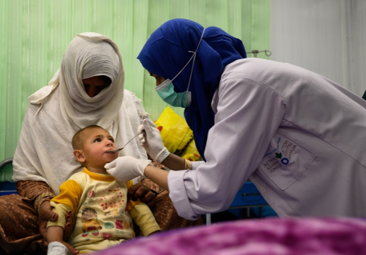 Medical staff feeding child with malnutrition while he is held by his mother.