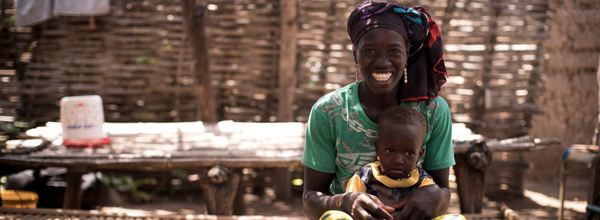 A smiling mother in Mali holds her child, supported by Action Against Hunger's community health workers to improve health.