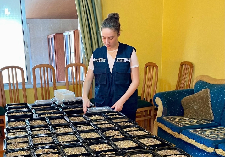 Woman lying out food and meals on table in room with yellow walls.