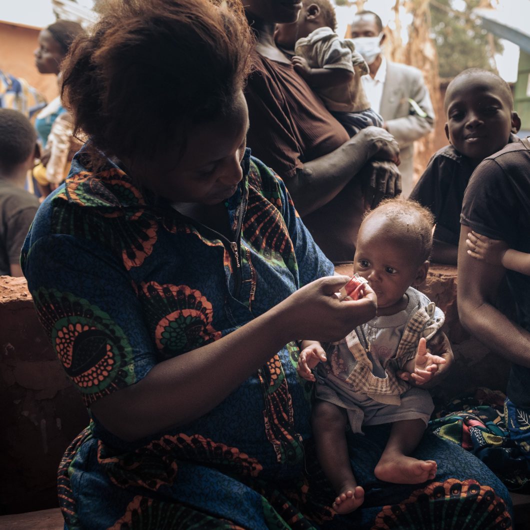 Women in Democratic Republic of Congo wearing colourful shirt feeding baby.
