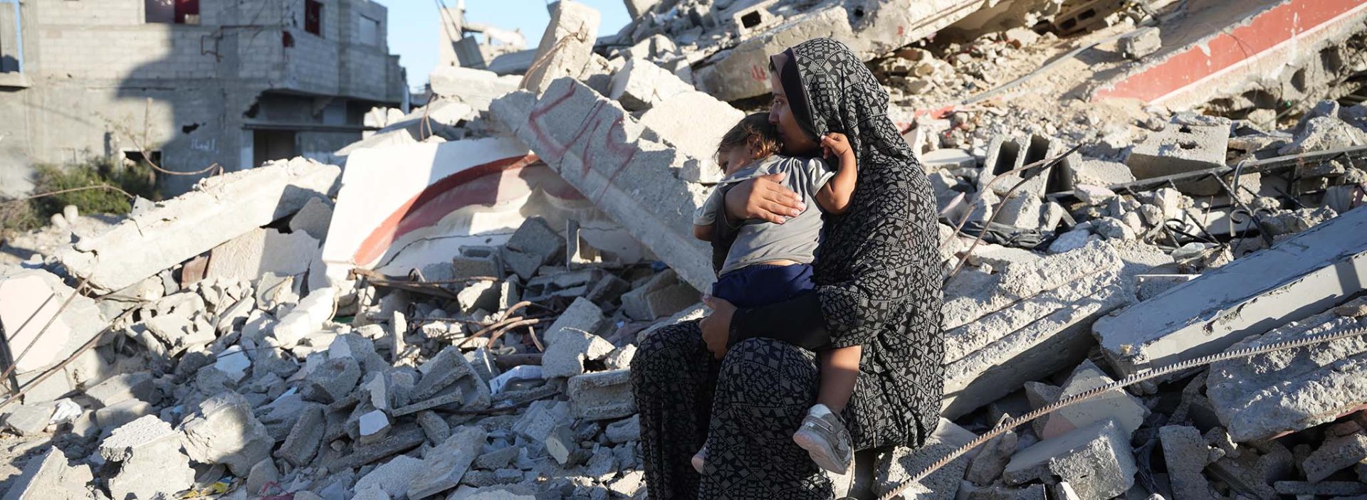 A woman holds her daughter on the remains of a damaged building in Gaza, October 2024.