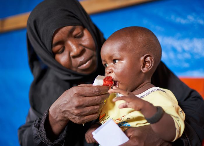 Sudanese woman feeds her baby food for malnutrition.